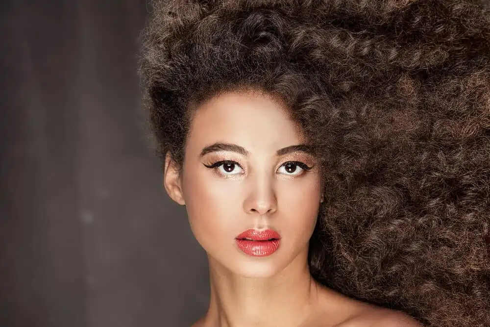 African American lady wearing black eyeshadow, red lipstick, and a synthetic hair wig over a wig cap.