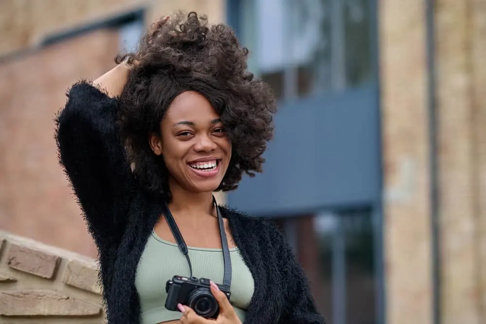 African American female with a big smile wearing a lace front wig with a black jacket and green t-shirt.