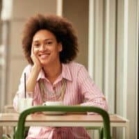 Cute girl having a cup of coffee with a medium skin tone wearing a wash and go hairdo on curly brown hair.