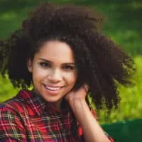 Cute African American female with an oval face wearing a medium-length layered haircut in a curly bob style.