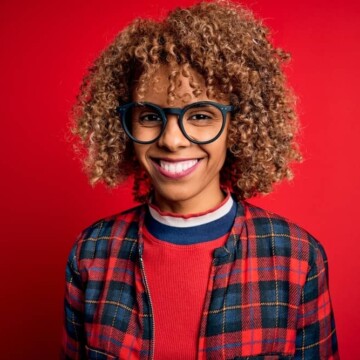 Cute black girl with chemically treated bleached hair follicles wearing a plaid jacket and black glasses.