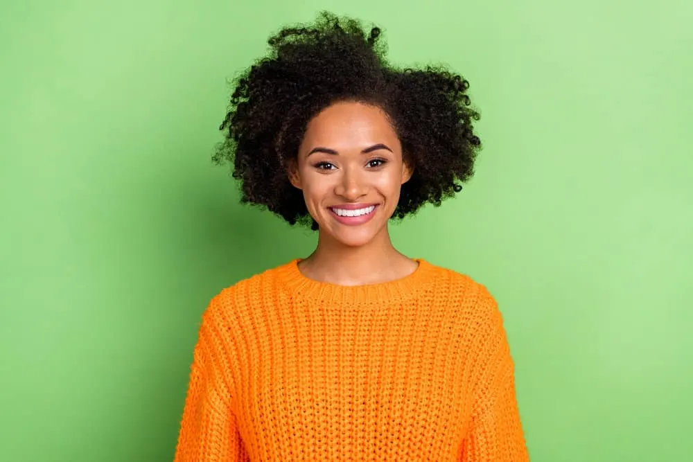 Optimistic black lady without any noticeable facial hair wearing a casual orange sweater on a chilly winter day.