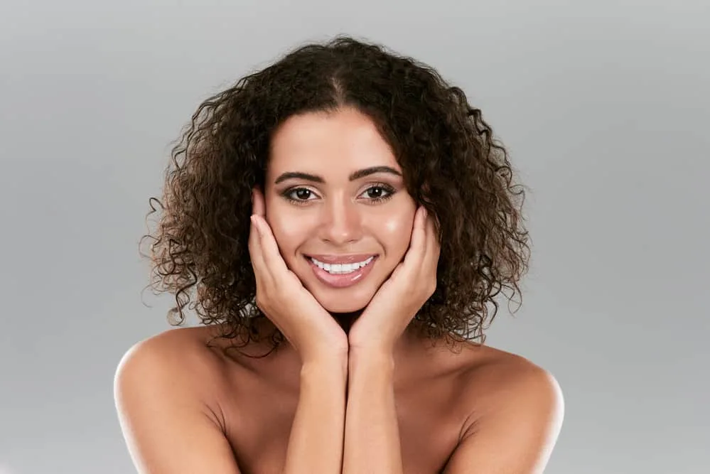 A female with mid-length oily hair from argan oil is holding her hands under her chin. 