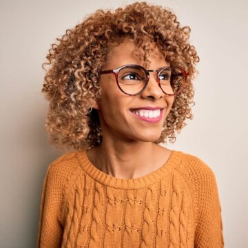 A black girl with a brown semi-permanent hair dye on her natural curls wearing a natural yuzu cranberry fragrance.