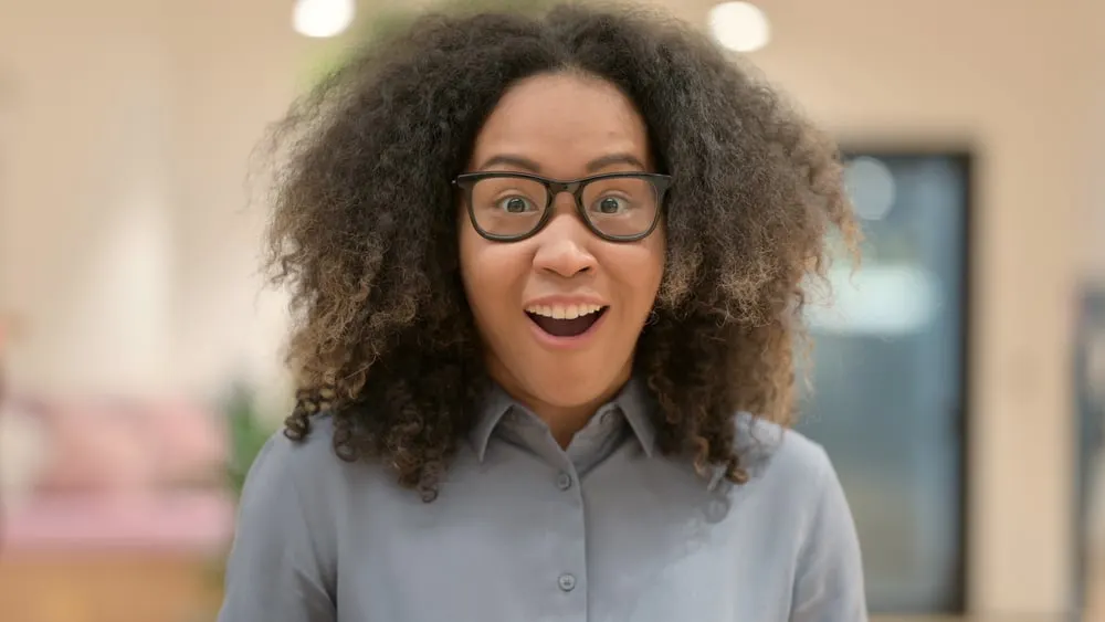 A surprised young black girl with an edgy wolf cut with an ombre hair coloring wearing a gray dress shirt.