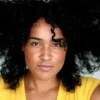 A young black woman with naturally curly hair gathered her loose hairs to keep her hair protected in a sleep bonnet.