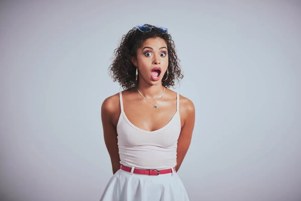 A beautiful female with wavy hair styled with a hair thickening serum wearing a white spaghetti strap shirt and skirt.