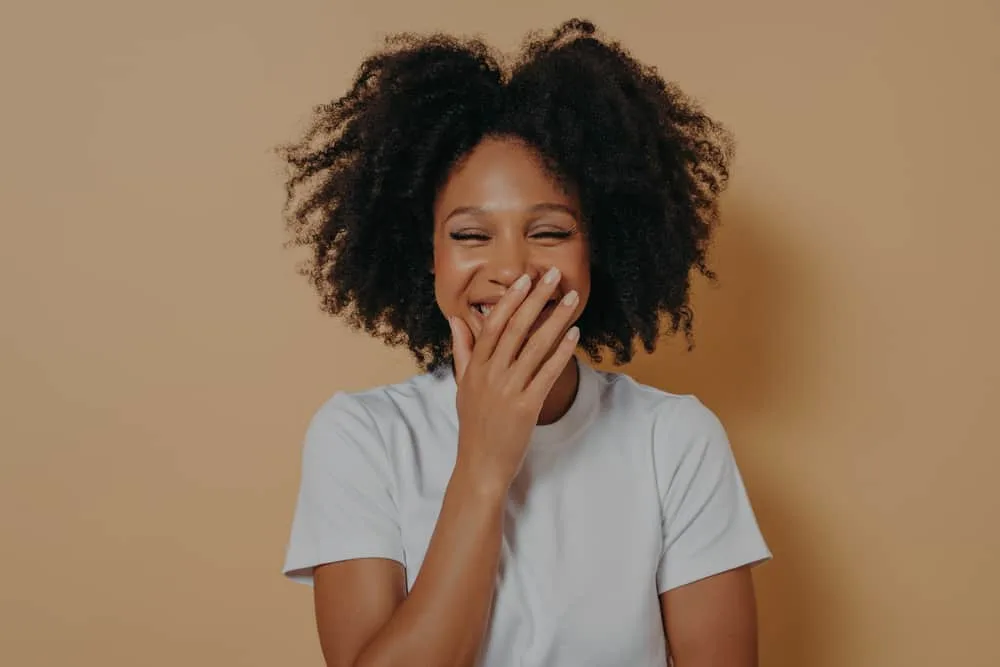 A cute dark-skinned lady with dark brown colored hair was laughing while covering her mouth.