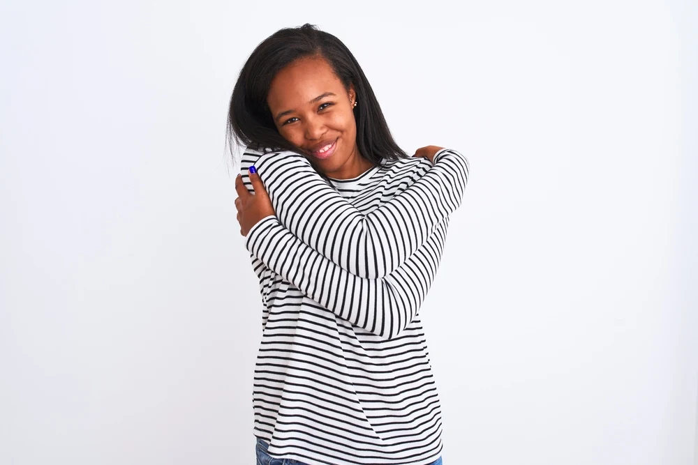 A cute black female after drying her wet hair is hugging herself and admiring her hair's health.