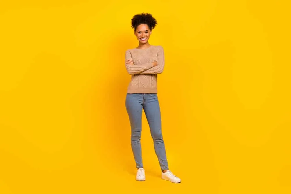 Beautiful young African lady wearing a light brown sweater and stone-washed blue jeans with white sneakers.