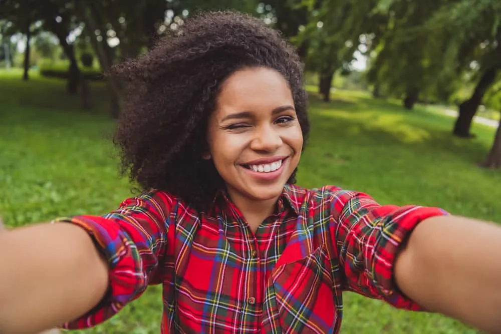 Teenage black girl with recently trimmed curls with thinning shears wearing pink lipstick is taking a selfie.