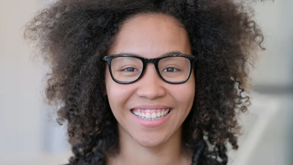 A smiling young African lady with fine hair wearing heavily layered hair creating volume around her ears.