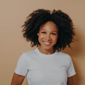 Young African American female whose wavy hair curls at then ends wearing a casual white t-shirt.