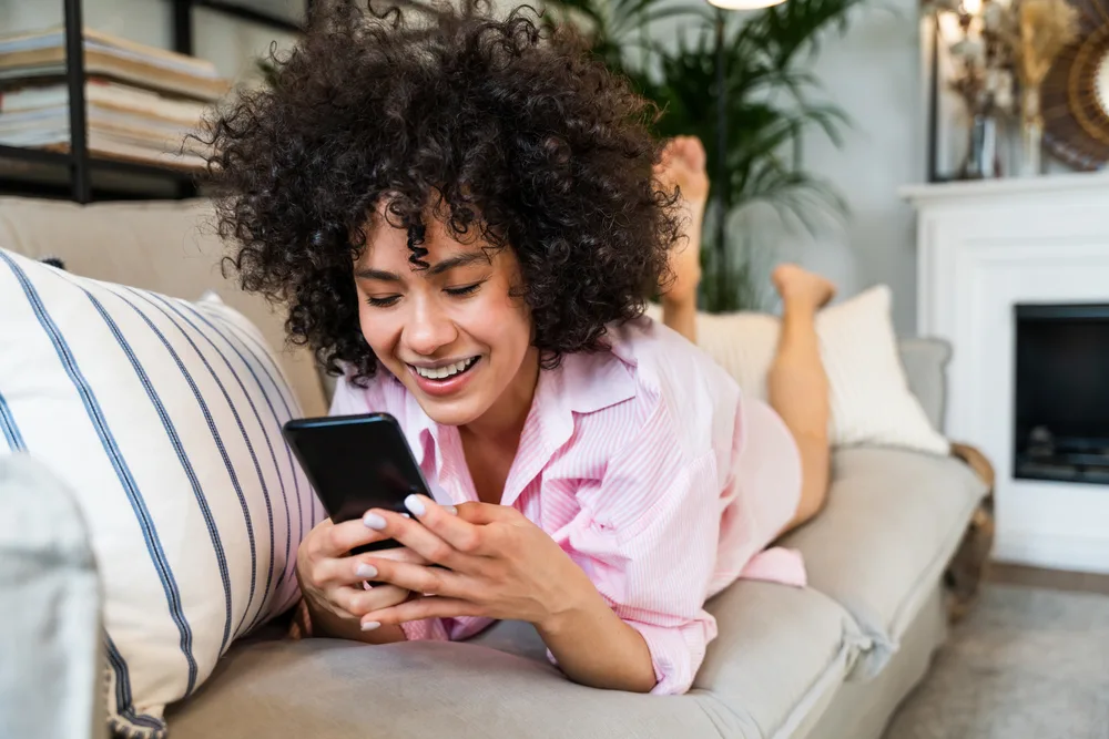 A lady with color-treated hair researched hair loss treatments on her iPhone 13 while relaxing on the couch.