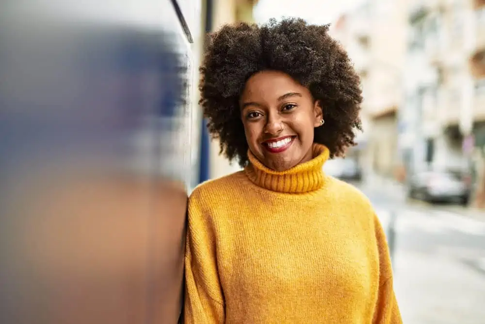 A pretty black lady after covering grey roots with demi-permanent dye wearing a yellow sweater.