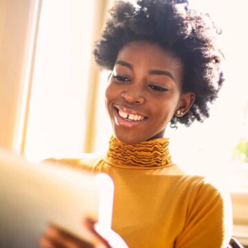 Dark-skinned black girl wearing an orange shirt trying a new hair style app before going to the hairdresser.