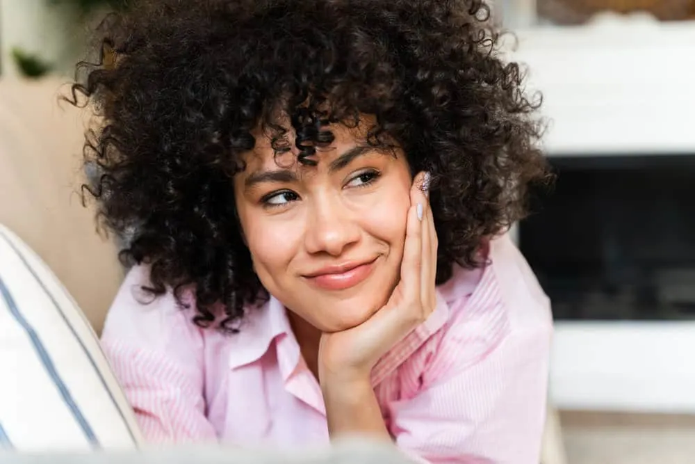 A lady with a confident smile wearing bouncy natural curls after using OGX Coconut Milk Shampoo.