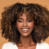 Young African lady with an oval face shape and kinky hair embracing the classic fringe bottleneck bang trend.