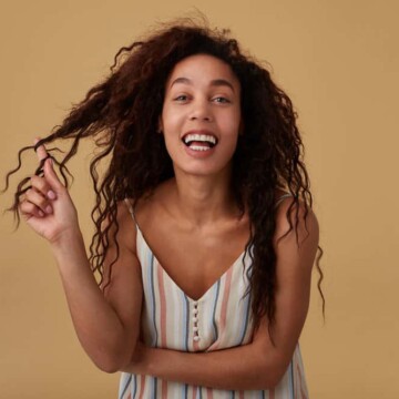 Joyful black female with thick hair and heat-free curls wearing her hair in bouncy waves after using low-heat tools.