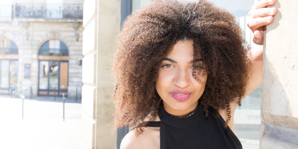 Cute African American girl with oily skin wearing red lipstick and bouncy natural curls after using massage oil.