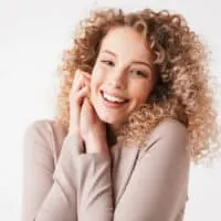 A cheerful young white girl with a dark brown natural hair color and a balayage hair-do on a medium hair length.