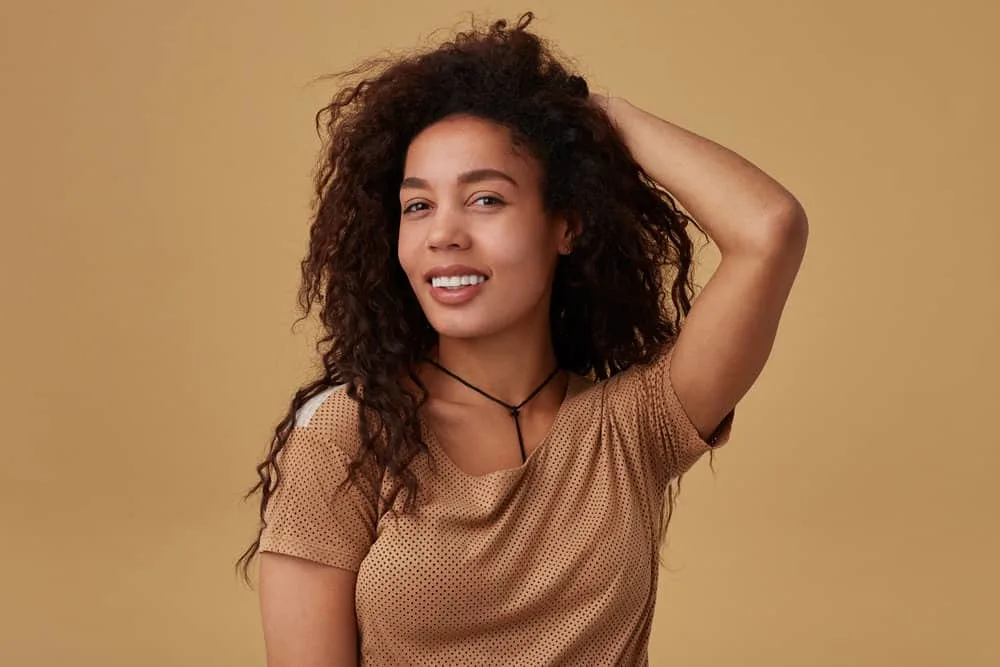 A mixed-race female wearing a beige polka-dot shirt with rough, dry hair styled with high heat tools for volume.