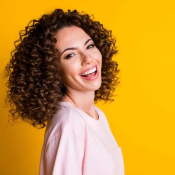 A white girl with flat iron permed hair created with normal hair styling techniques looks back at the camera.