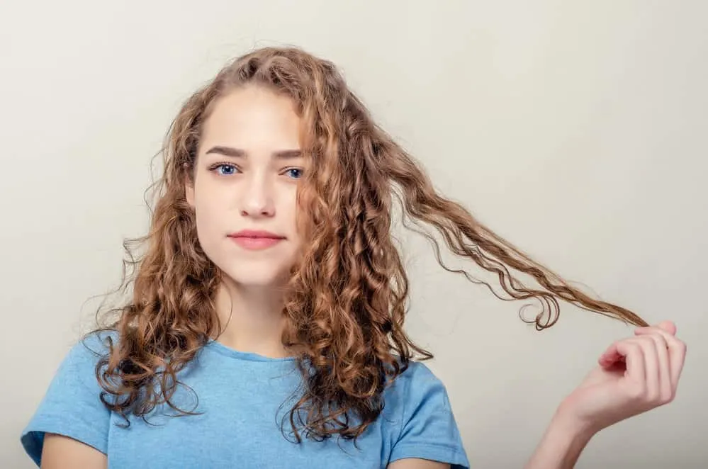 A female with blue eyes wearing red lipstick with coily hair styled with curl creams and a coconut oil styling product.