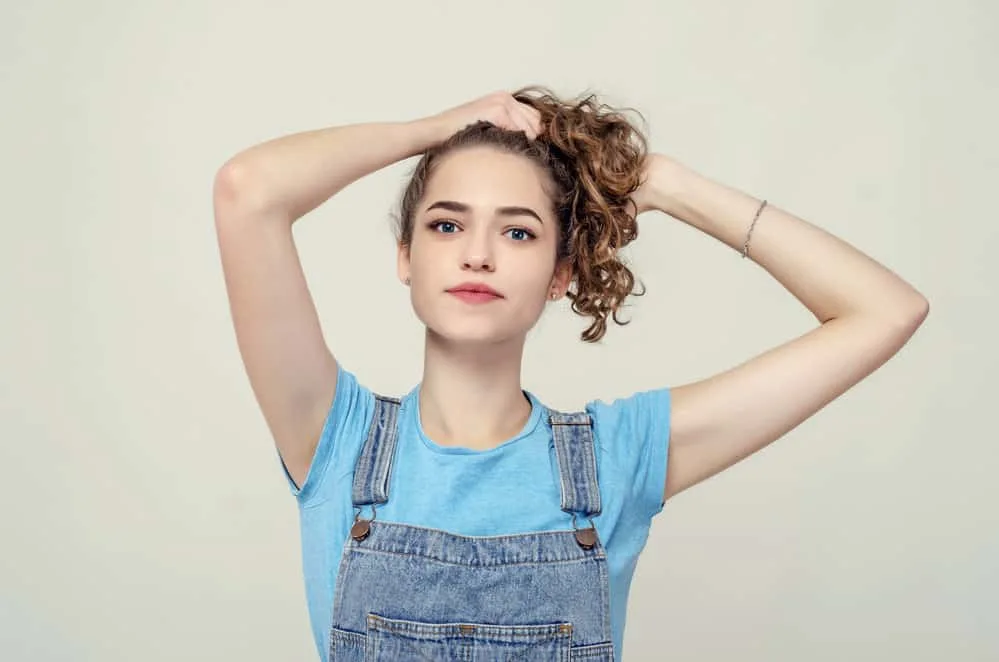 An attractive girl with densely packed waves is preparing to pineapple her hair for tighter curls.