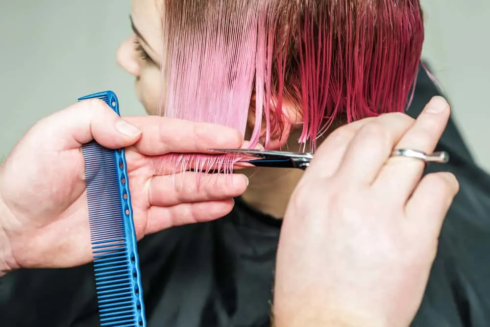 Professional hairstylist cutting a lady's hair after using liquid laundry detergent and a cotton pad to remove dye stains.