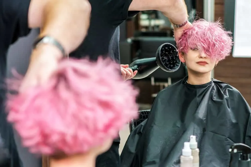 A cute white girl getting her hair blow dried with a diffuser to dry hair dye after undergoing a hair coloring treatment.