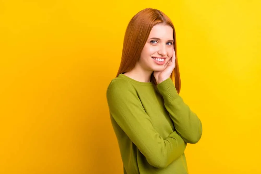 A young white woman in a green sweater has fine hair styled with Curly Girl-approved hair products.