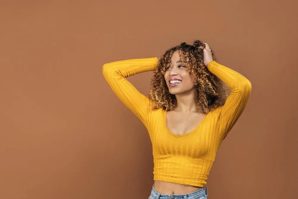 A cheerful young lady poses after using hair masks and darker hair dye on her uneven bleaching outcome.