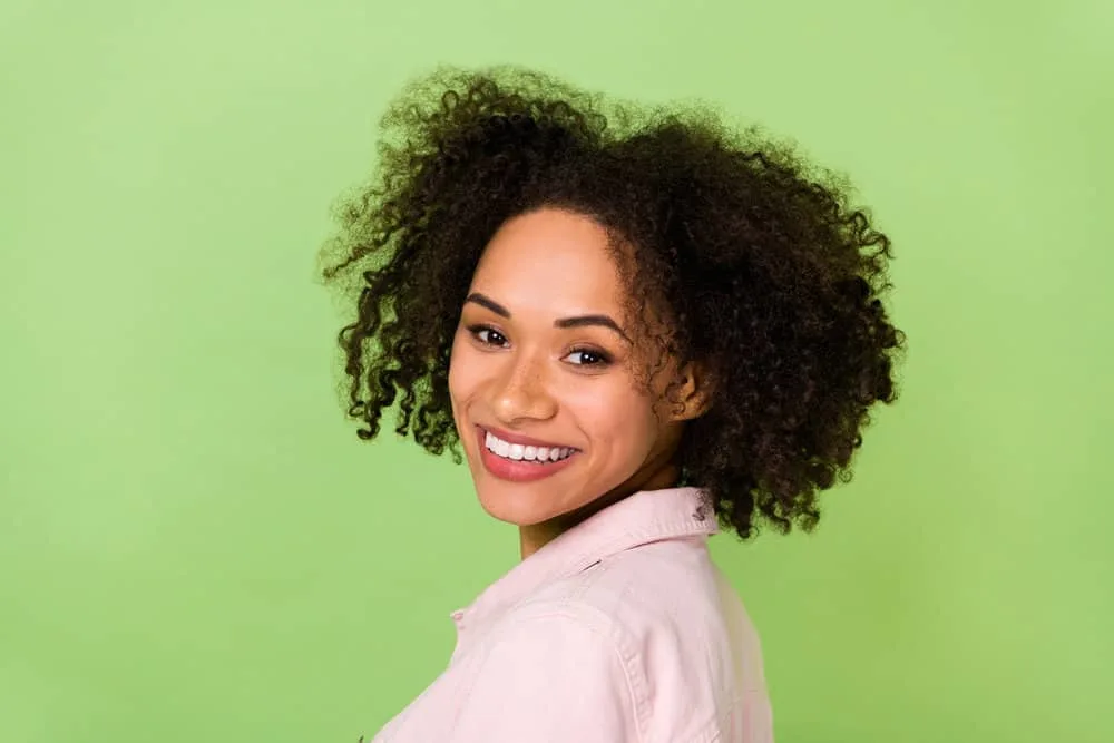 A black woman with curly hair strands treated with a hair mask to restore moisture and a protein treatment.