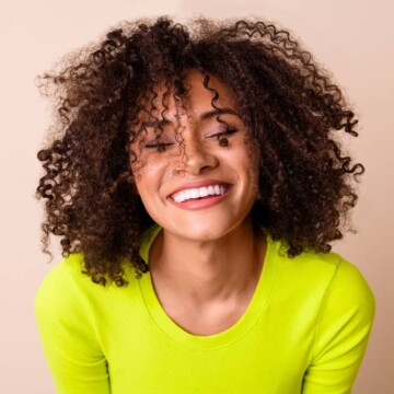 A cute curly girl with frizzy hair washed with mimosa flower shampoo, a leave-in smoothie cream, and coconut water.