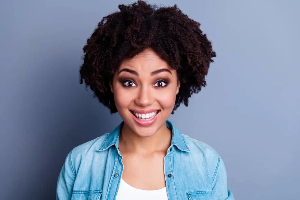 A young African female that takes a fish oil supplement decided to towel dry her damp hair after a cleansing routine.