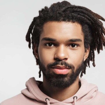 A young African man with traditional locs that are a mid-neck hair length on a 4B hair texture / medium hair density.