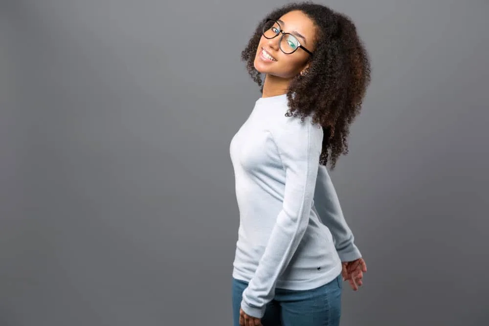 A young black lady wearing a casual blue shirt and jeans with an ombre hairdo with dark brown and black hair strands.