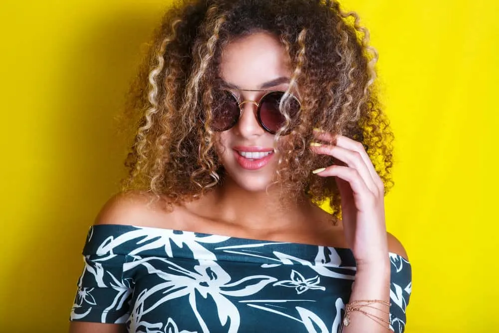 A young black girl with very dark hair wearing face-framing highlights on her naturally curly hair strands.