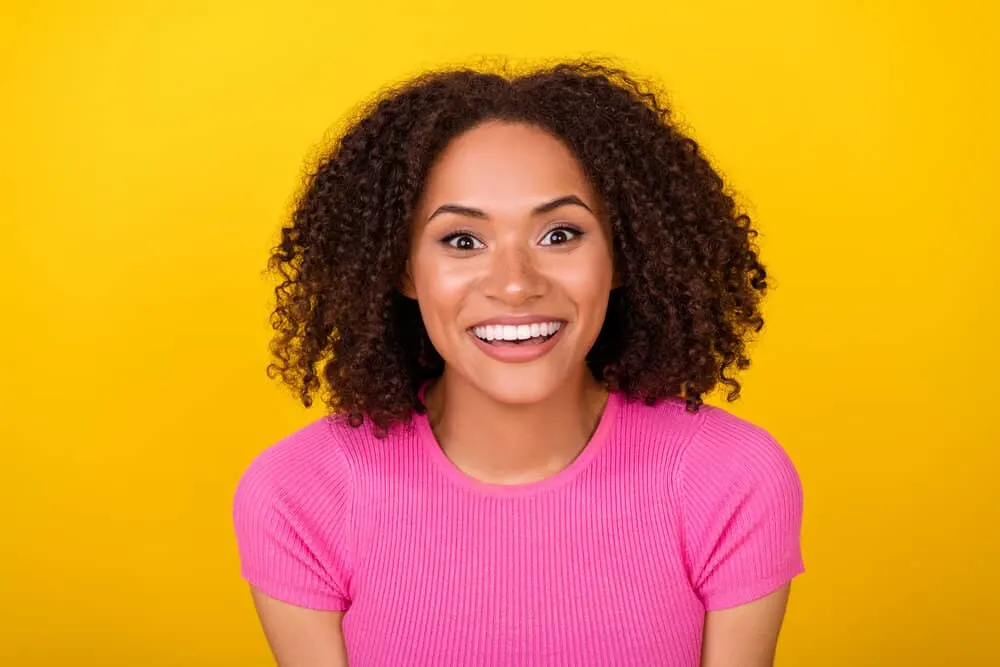 A cheerful young female wearing her curls in a shoulder-length wash-n-go style after letting her hair dry naturally.