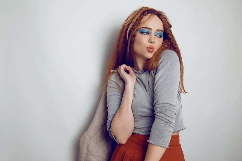 A cute white female crimped her hair with a flat iron before letting her hair cool while wearing a stylish outfit.