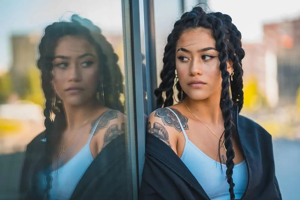 A fine young woman with beautiful olive skin and flower shoulder tattoo wearing her black hair in rope braid hairstyle.