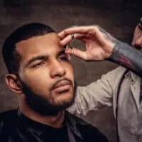 A man in a barber shop getting a quality haircut on his 2C straight hair with an electric trimmer and scissors.