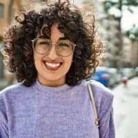 A cute middle eastern female with frizzy hair is experiencing hair breakage and stray hairs due to her hair care routine.