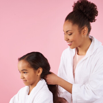 African American mother styles her daughter's damp hair with velcro rollers to bouncy curls without a hair dryer.