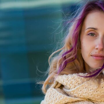 A female with a purple and dark blonde hair color has leftover hair dye on her stained skin from an at-home dye job.