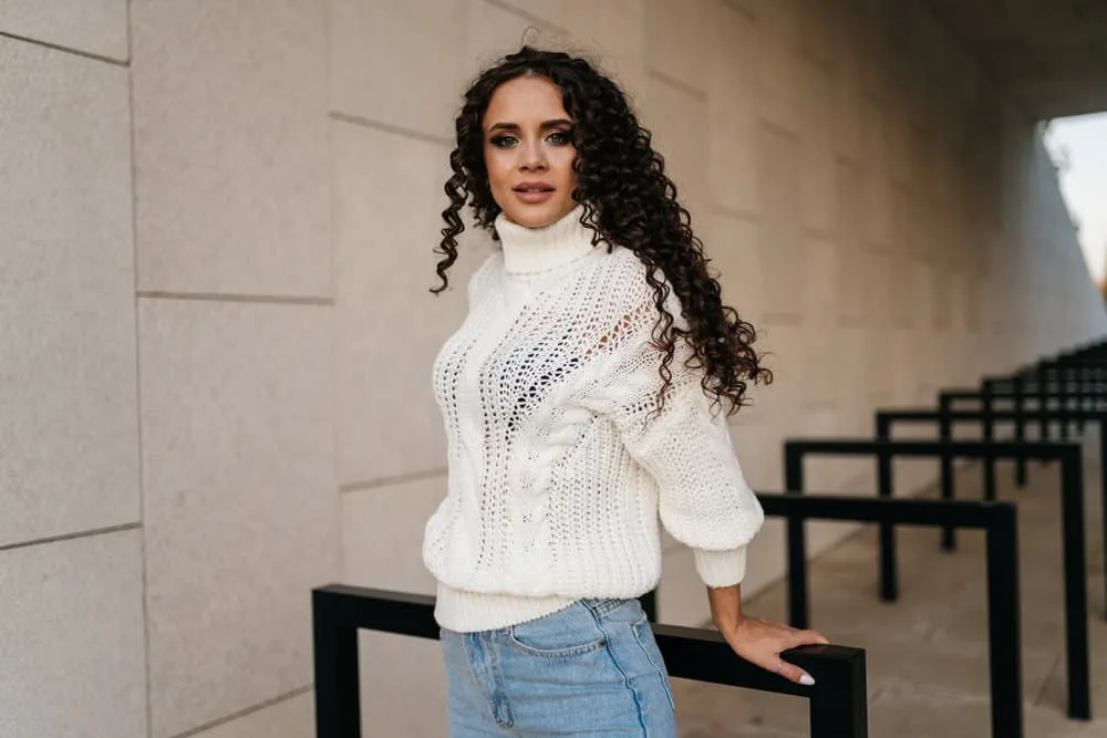 A stylish girl wearing a casual white sweater is leaving a hair salon after getting a hot perm solution.