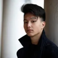 A young adult male is wearing popular Korean messy hair that has been brushed forward with a wavy texture.