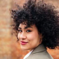 A young Latin female with thick hair used a boar bristle hair brush to style her type 3 curly hair strands.