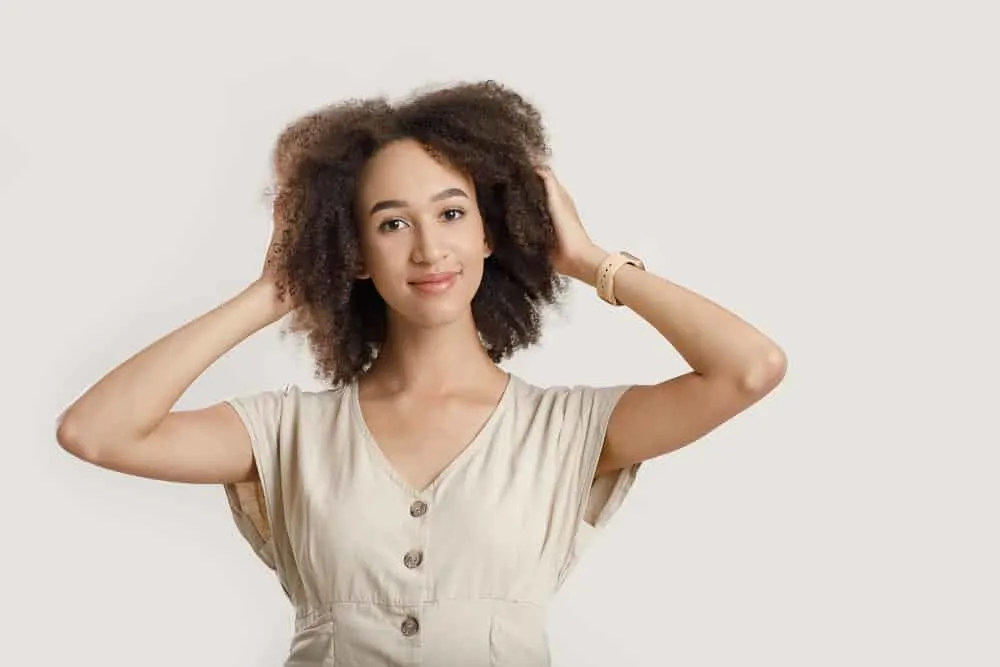 A light-skinned African American female with type 3C natural curls wearing a beige dress with an Apple watch.